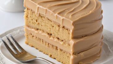 A slice of peanut butter cake with honey frosting on a plate, highlighted by soft lighting