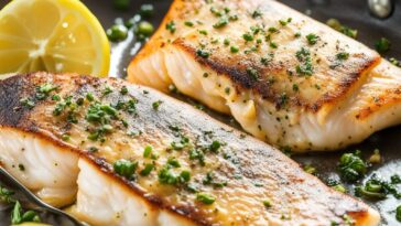 Golden-brown pan-seared fish fillet on a white plate with lemon garnish